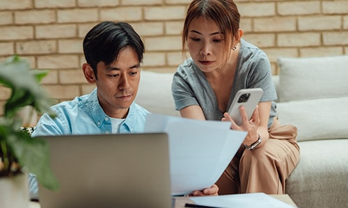 Man and woman reviewing documents with a smart phone and laptop.